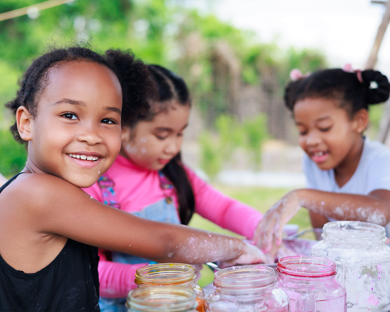 Three little girls doing crafts with jars outdoors. Project L.E.A.P child care summer camp